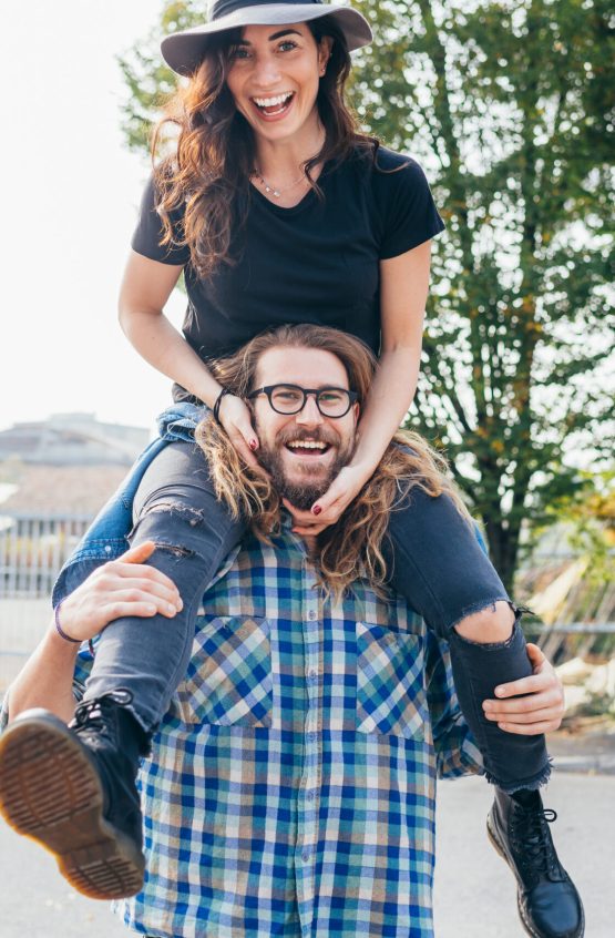 Young beautiful happy woman shoulder riding her bearded boyfriend outdoor throughfare - celebration, good news, happiness concept